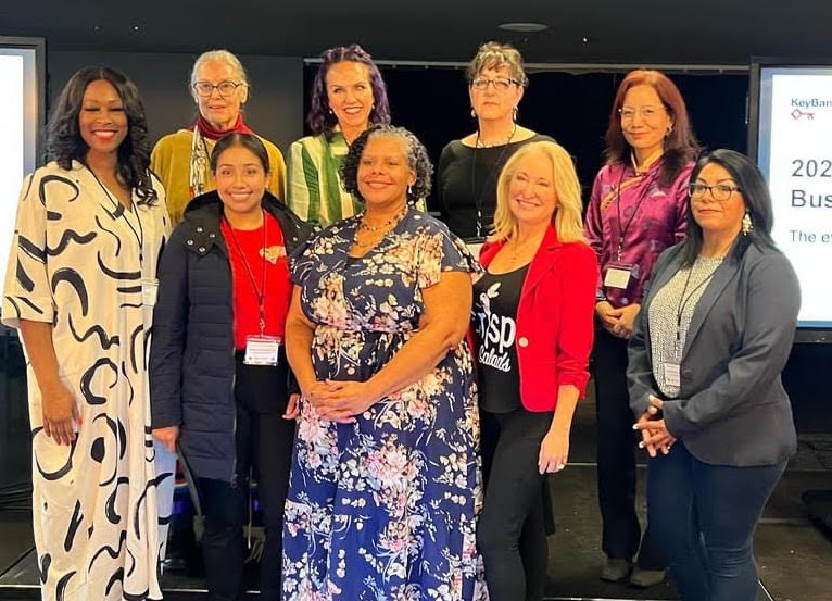 Adesina of Ventura Home Loans stands with other winners of Key4Women Pitch Contest. Image description: 9 women business owners stand together on stage in business attire to celebrate their pitch contest win.